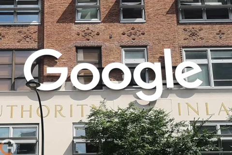 Large white 'Google' sign mounted on a brick storefront with windows above the sign. A curved streetlamp is visible in the foreground.