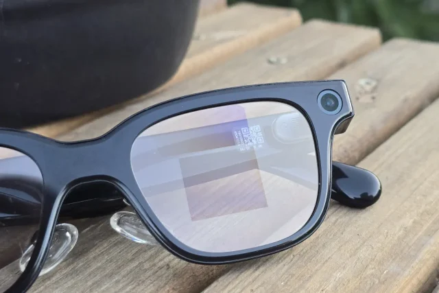 Black smart glasses with a small built-in camera at the temple resting on a wooden surface.
