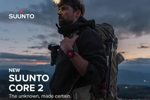 Hiker with a large backpack and red-dial Suunto Core 2 watch gazes over a valley at sunset, Suunto logo in the corner.